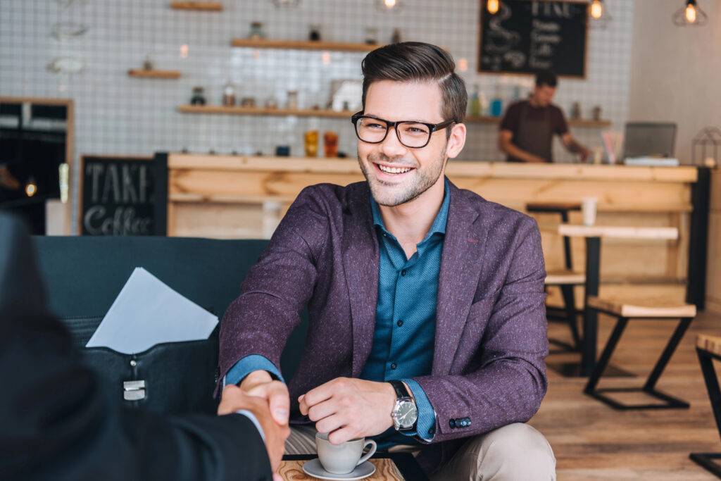 Business man smiling shaking hands while closing a deal at a coffee shop.