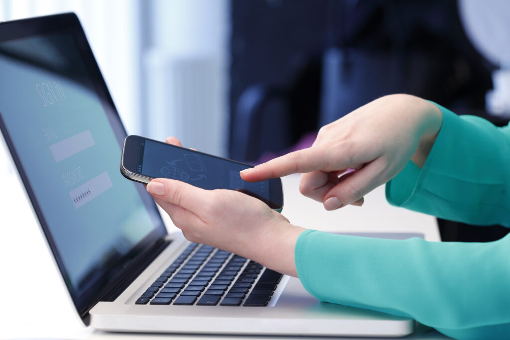 Close-up of a woman's hands on a laptop and using her mobile phone.