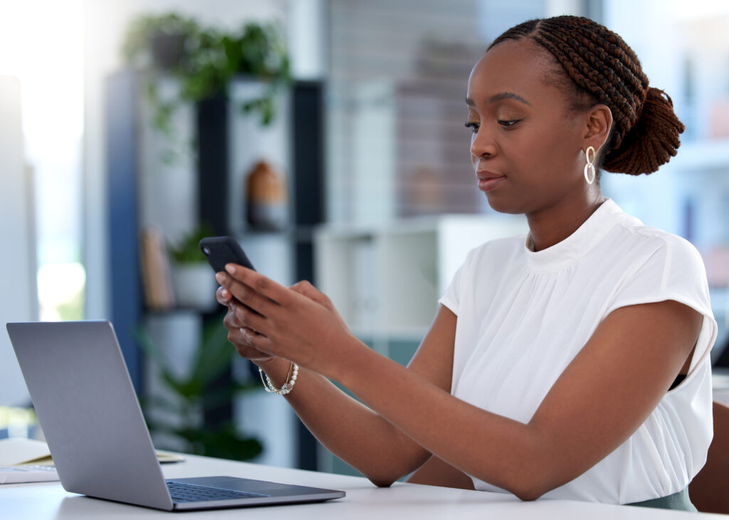 Woman browsing on phone in front of computer comparing cover letter writing servcies.