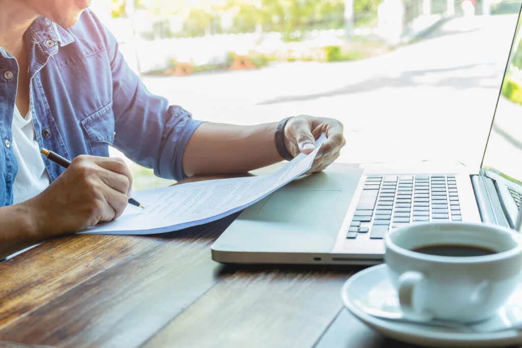 Businessman holding a cover letter and pen while sitting at laptop with a coffee.