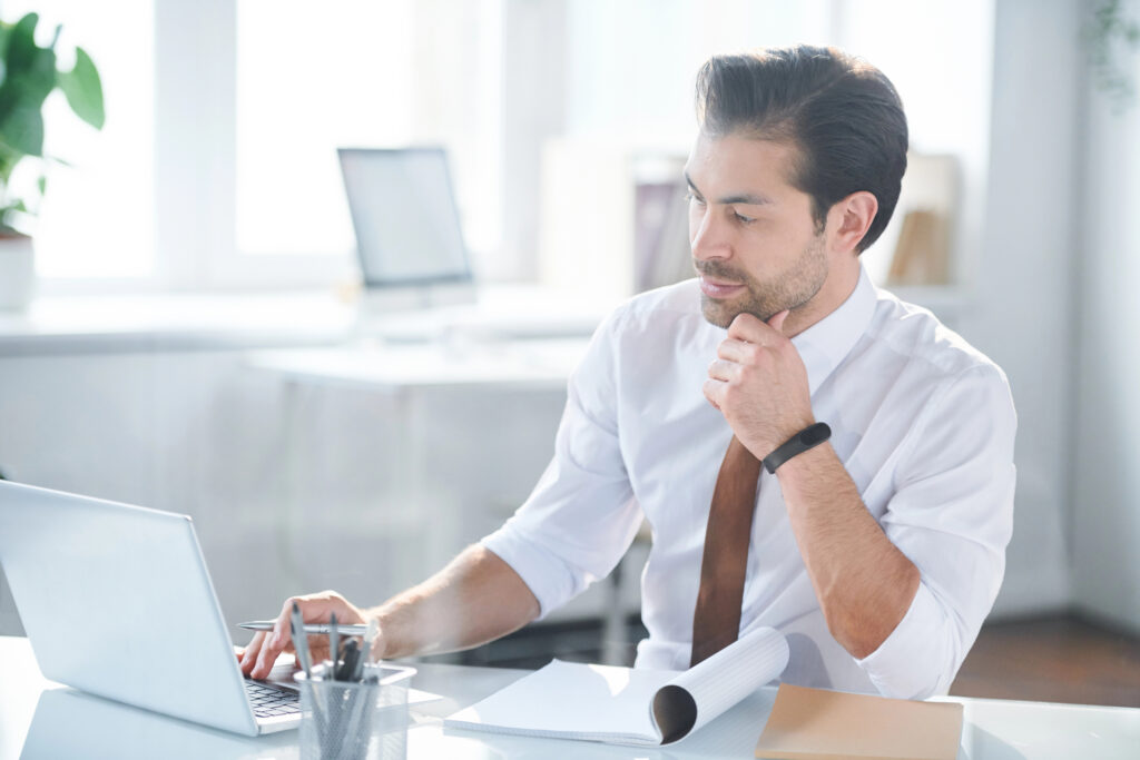 Man looking at laptop while writing his resume.